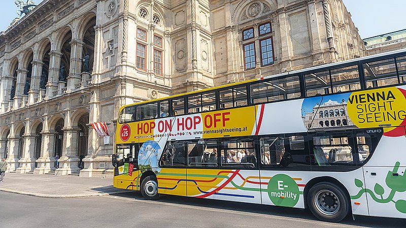 Red hop-on hop-off sightseeing bus traveling through the streets of Vienna past historic buildings