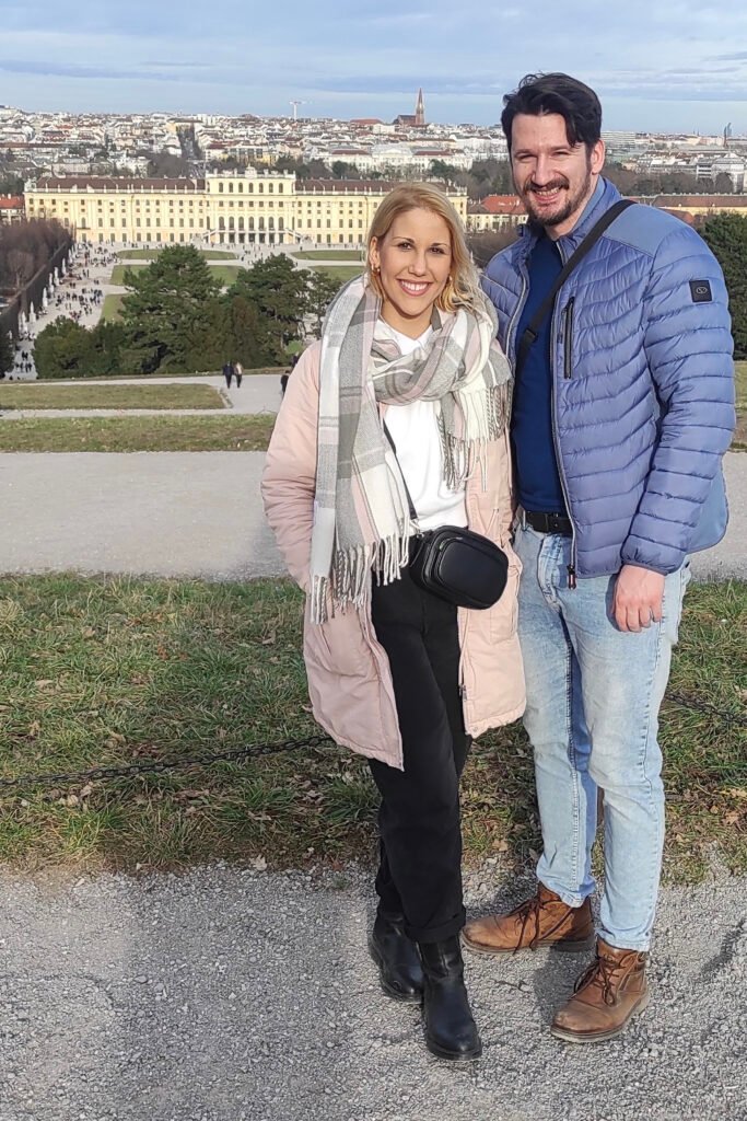Two travelers standing in front of the Schönbrunn Palace with baroque façade and gardens in background