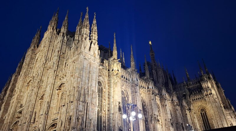 Duomo di Milano illuminated at night, with its Gothic spires and facade glowing against the dark sky.