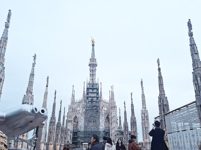 Madonnina and surrounding statues on the rooftop terrace of Duomo di Milano, overlooking the city skyline.