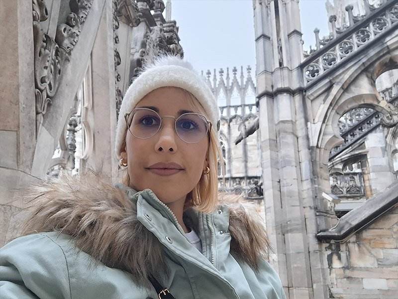 Traveler standing on the rooftop of Duomo di Milano, with the cathedral’s intricate spires and Gothic architecture visible in the background.