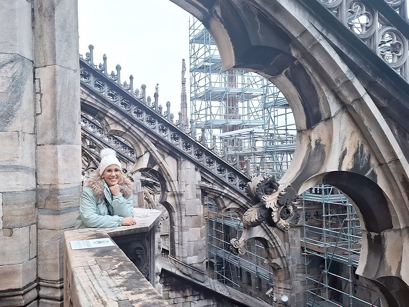 Traveler standing on the rooftop of Duomo di Milano, with the cathedral’s intricate spires and Gothic architecture visible in the background.