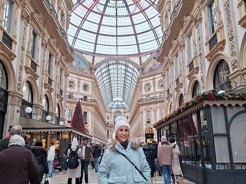 Traveler standing in the center of Galleria Vittorio Emanuele II in Milan, with the central Christmas tree and the iconic glass dome and historic architecture in the background.