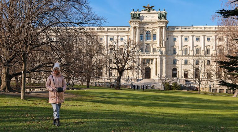 Woman walking through Burggarten Park with the Neue Burg building of Hofburg Palace in Vienna, Austria.
